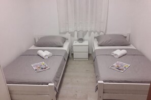 A twin room with two beds, a nightstand with a lamp, and a window with sheer curtains. - Batur Pool Apartments (Zadar)