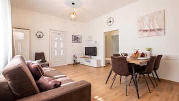 Een moderne woonkamer met een bank, een eethoek met stoelen, een televisie en kunstwerken aan de muren.