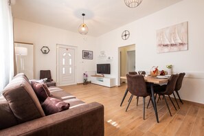 A modern living room with a sofa, a dining area with chairs, a TV, and artwork on the walls. - Batur Pool Apartments (Zadar)