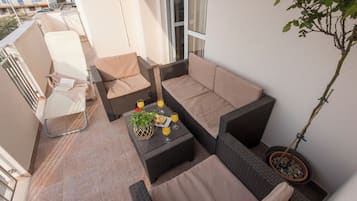 Ein Balkon mit Korbmöbeln, einer Topfpflanze und einem Tisch mit einem Glas Orangensaft.