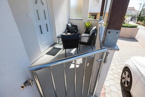 Une entrée fermée par un portail en métal, une porte blanche et un petit espace extérieur aménagé avec deux chaises et une table.