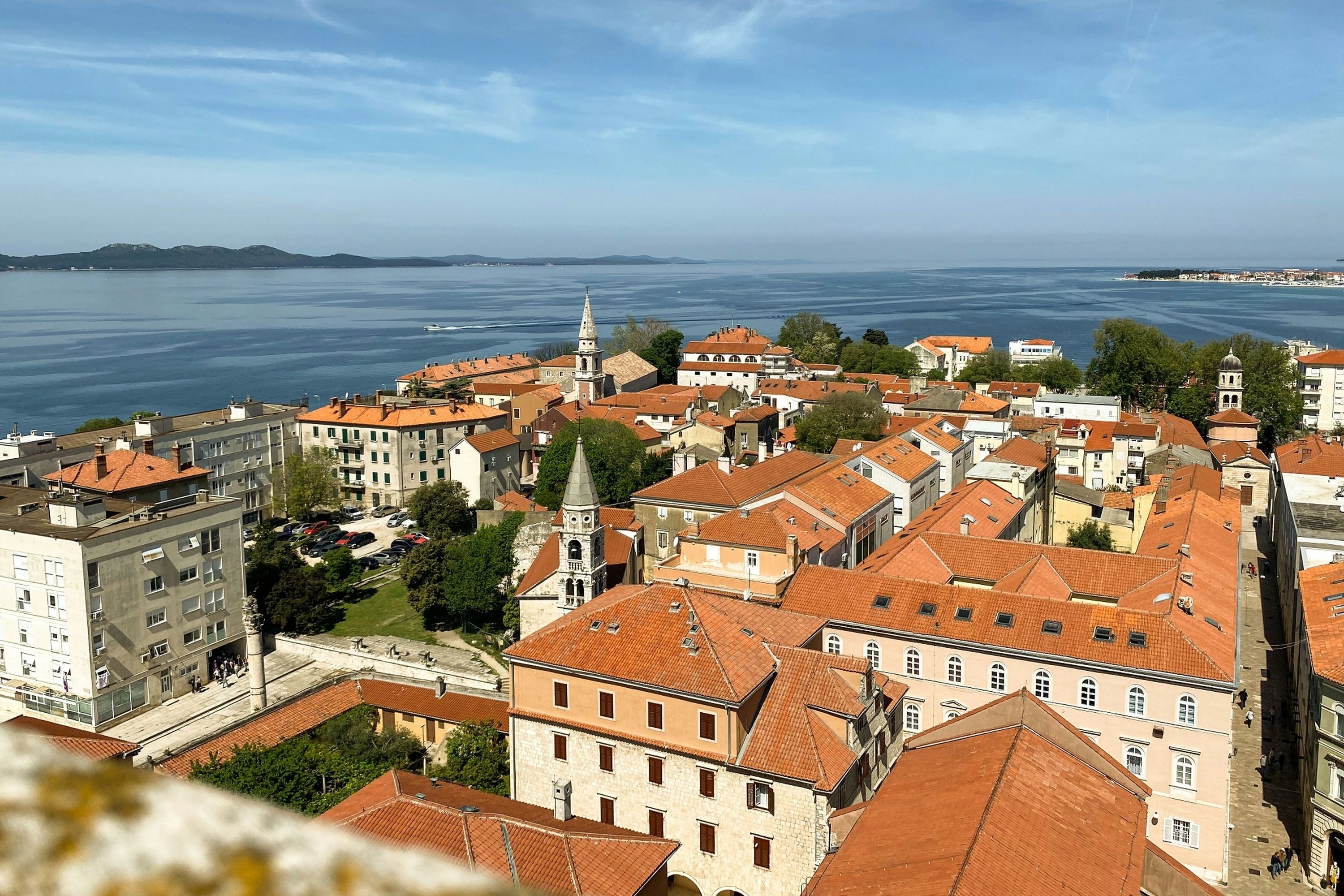 A coastal cityscape with historic buildings, a prominent church tower, and a view of the sea.