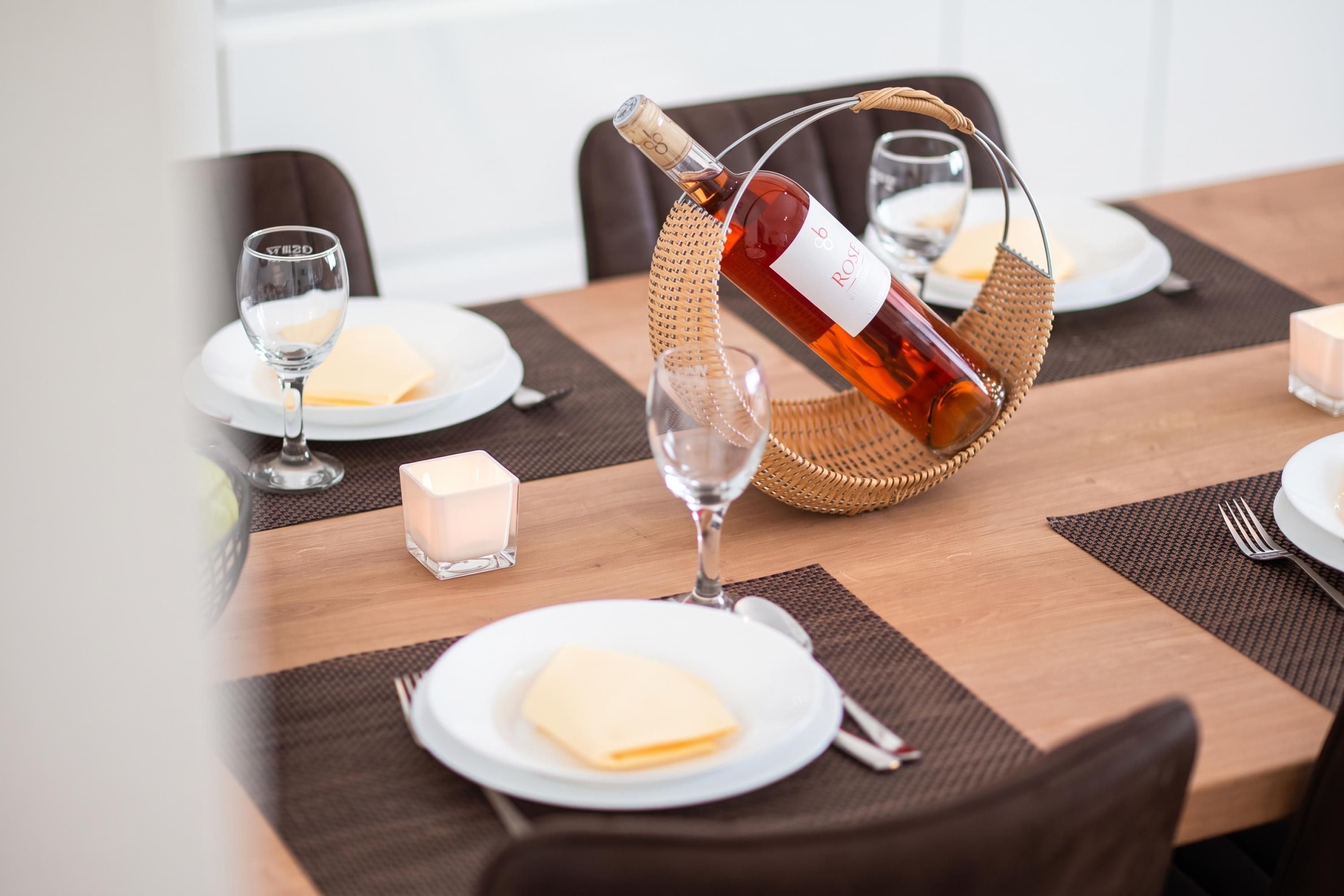 A dining table set with plates, glasses, a bottle of wine, and a candle.