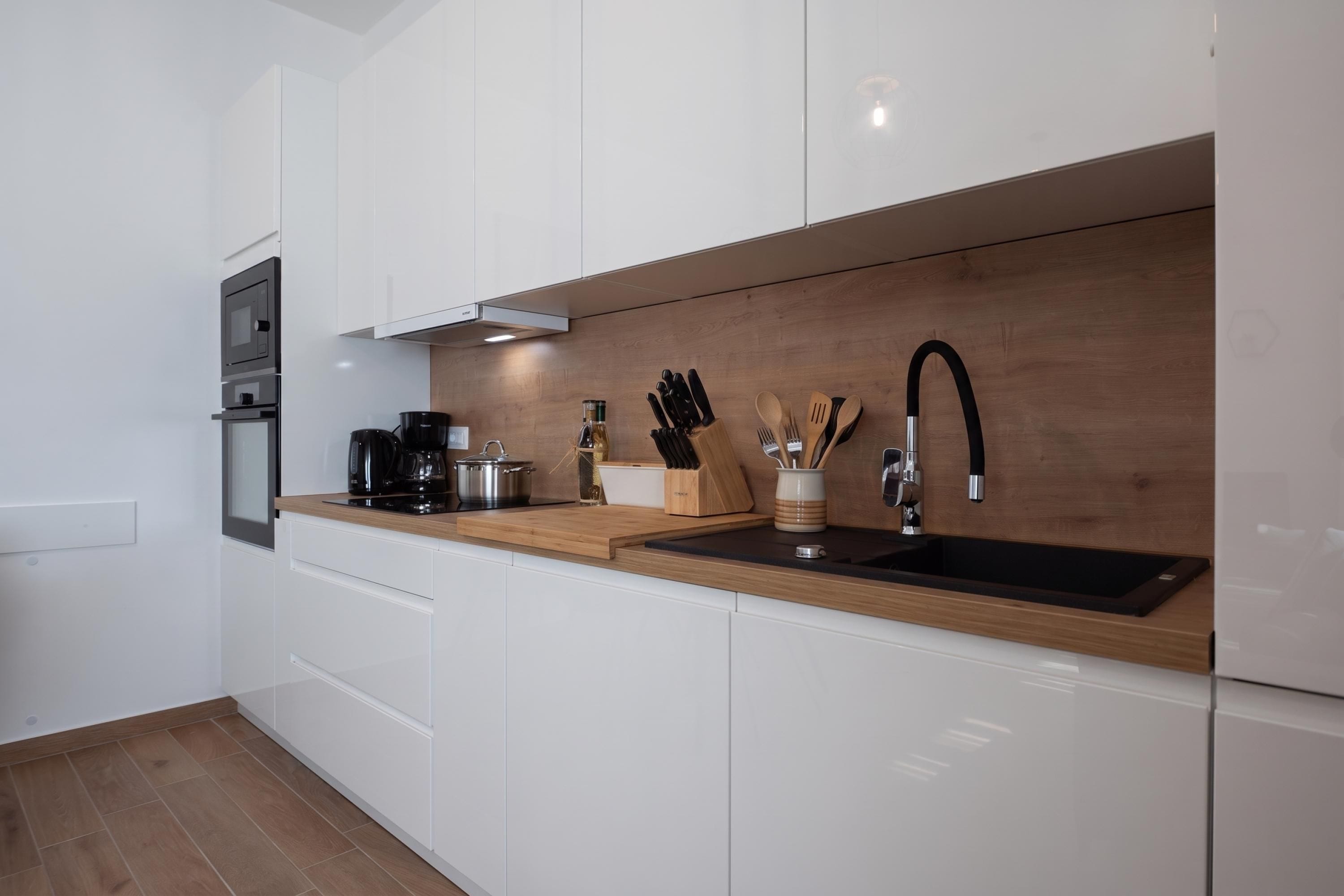 Een moderne keuken met witte kastjes, een houten aanrecht, een zwarte spoelbak en roestvrijstalen apparatuur.