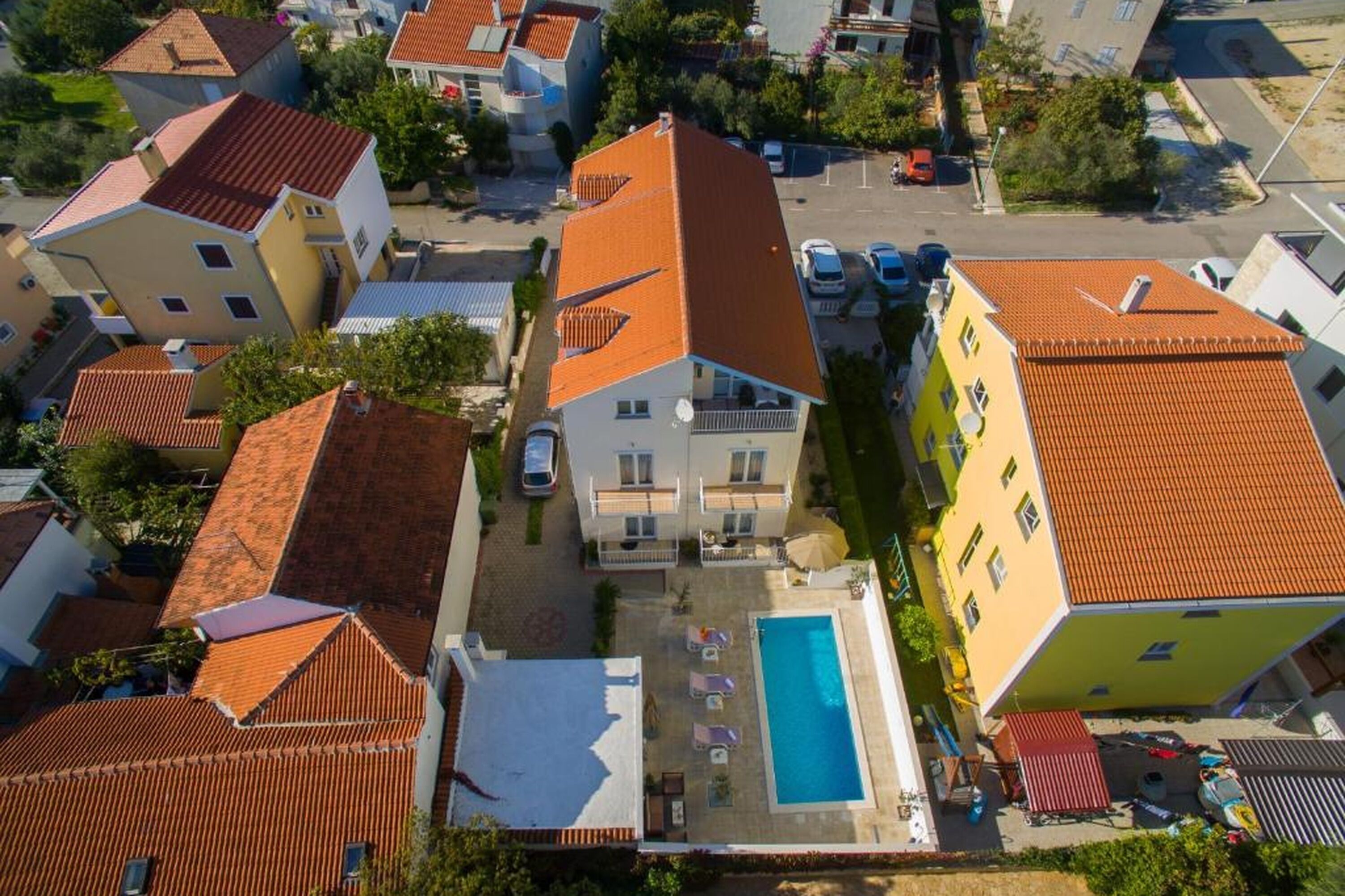A residential area with a swimming pool, multiple buildings with red-tiled roofs, and a clear sky.
