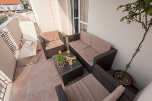 A balcony with wicker furniture, a potted plant, and a table with a glass of orange juice. - Batur Pool Apartments (Zadar)