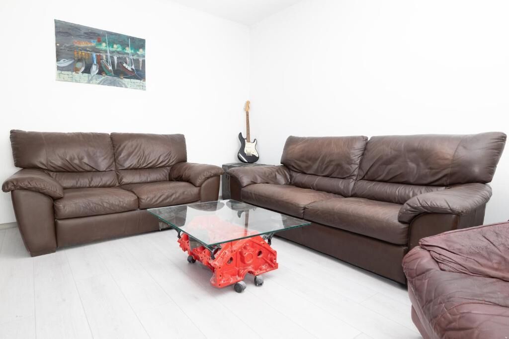 A living room with two brown leather sofas, a glass coffee table, and a guitar.