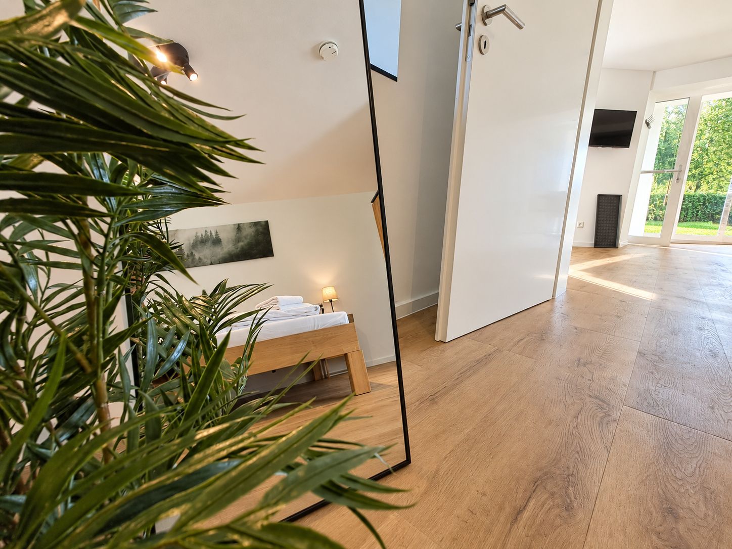 Ein modernes Hotelzimmer mit Holzboden, einem Bett mit weißen Leinen, einer Nachttischlampe und einem Gemälde an der Wand.