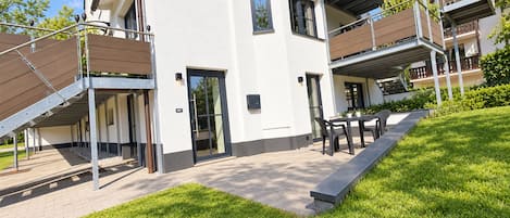 A modern building with a covered outdoor seating area and a grassy lawn.