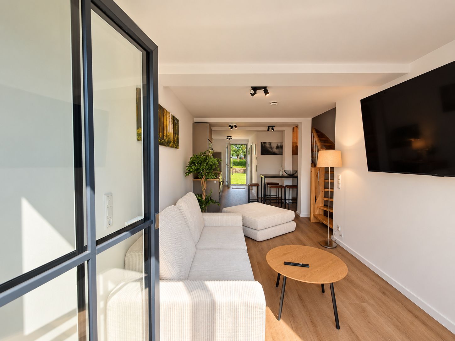 Ein modernes Wohnzimmer mit einem Ecksofa, einem runden Holztisch und einem an der Wand montierten Fernseher.