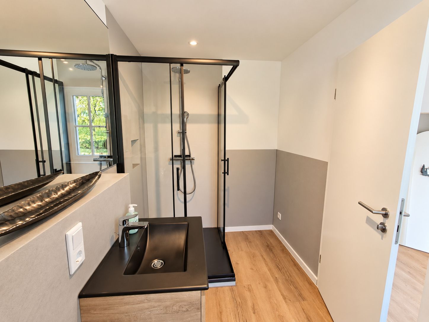 A modern bathroom with a glass shower enclosure, a sink with a black countertop, and a wooden floor.