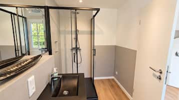 A modern bathroom with a glass shower enclosure, a sink with a black countertop, and a wooden floor.