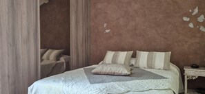 Un dormitorio con cama, almohadas, una mesita de noche y un velador.
