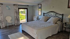 A bedroom with a bed, a chair, a nightstand, a lamp, and a window with a view. - Villa Dans le Golfe de Saint-tropez (Cogolin)