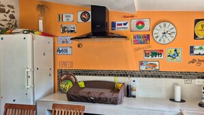 A kitchen with a stone wall, a refrigerator, a coffee machine, and various wall decorations including flags and a clock. - Villa Dans le Golfe de Saint-tropez (Cogolin)