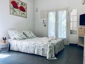 Een slaapkamer met een bed, nachtkastje, stoel, televisie en raam.