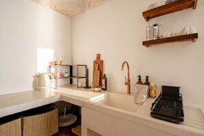 Una cucina con un piano di lavoro bianco, un lavello, una mensola in legno con utensili da cucina e un espositore nero per piatti.