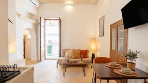 A living room with a sofa, coffee table, and TV. There is a dining table with placemats and a potted plant. - Casa Adamare - Charming Luxury Stay (Ostuni)