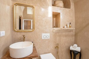 A bathroom with a large oval sink, a mirror with a gold frame, a towel rack, and a shelf with toiletries. - Casa Adamare - Charming Luxury Stay (Ostuni)