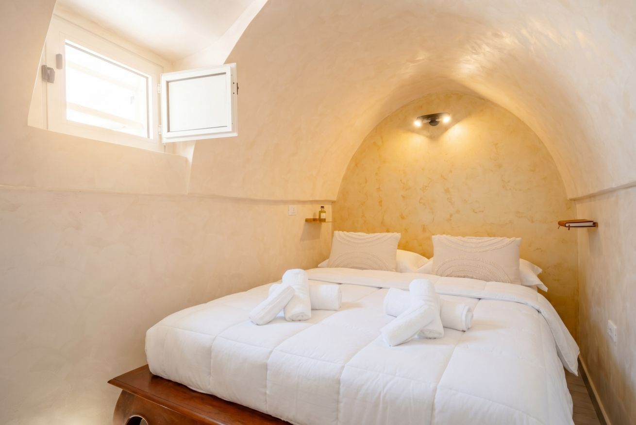 Una camera da letto con soffitto a volta, un letto con lenzuola bianche e una finestra.
