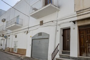 Un edificio bianco con un portone in metallo, una porta in legno e un balcone con ringhiera metallica.