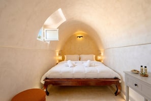 Quarto com cama de madeira, uma pequena janela e mesa de cabeceira com produtos de higiene pessoal.