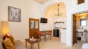 A living room with a sofa, a dining area with chairs, a kitchen with a TV, and a bathroom with towels. - Casa Adamare - Charming Luxury Stay (Ostuni)