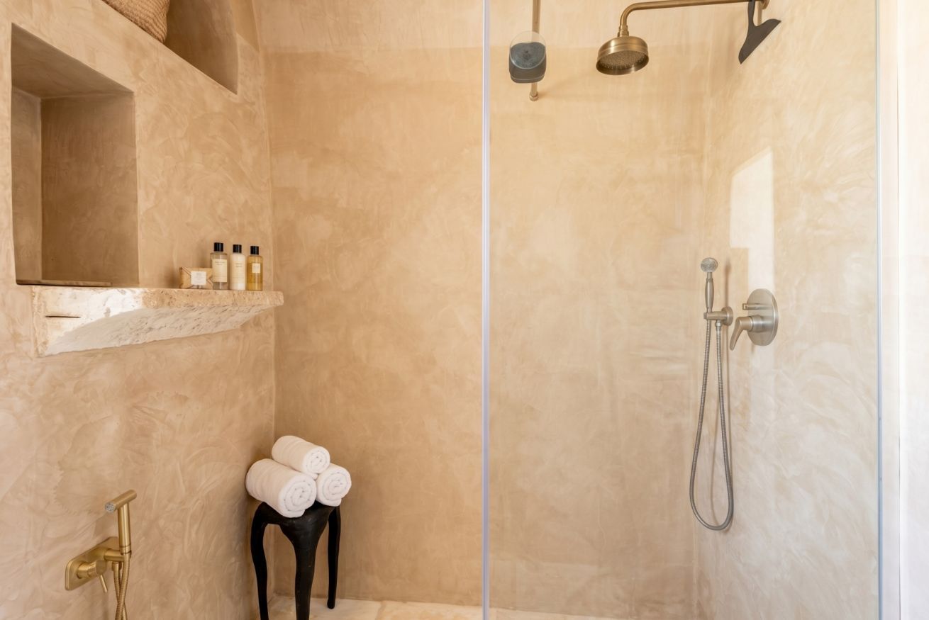 A walk-in shower with a glass door, a towel rack with towels, a shelf with toiletries, and a handheld showerhead.