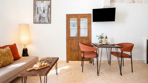 A living room with a sofa, a table with a lamp, a wooden door, and a TV mounted on the wall. - Casa Adamare - Charming Luxury Stay (Ostuni)