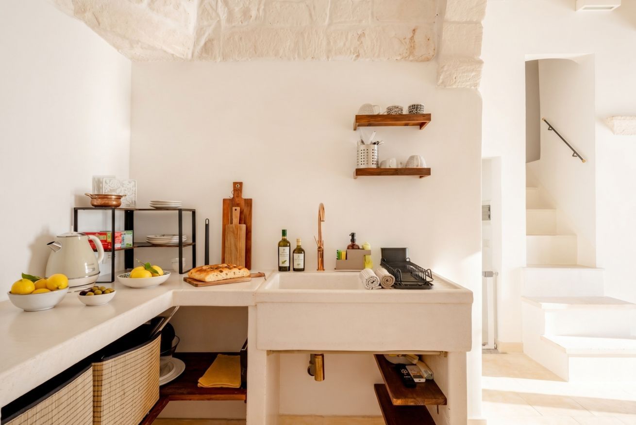 Una cucina con un piano di lavoro bianco, un lavello e una mensola in legno sopra.