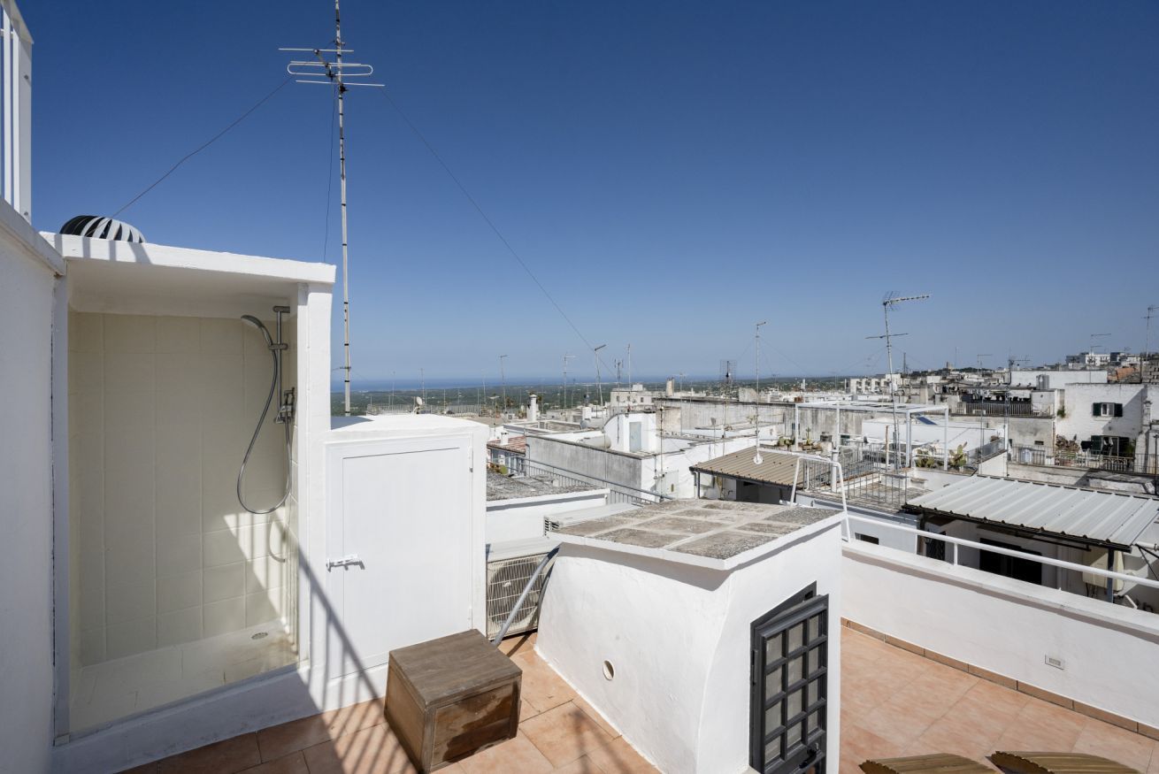 A rooftop terrace with a glass enclosure, a wooden stool, and a metal railing.