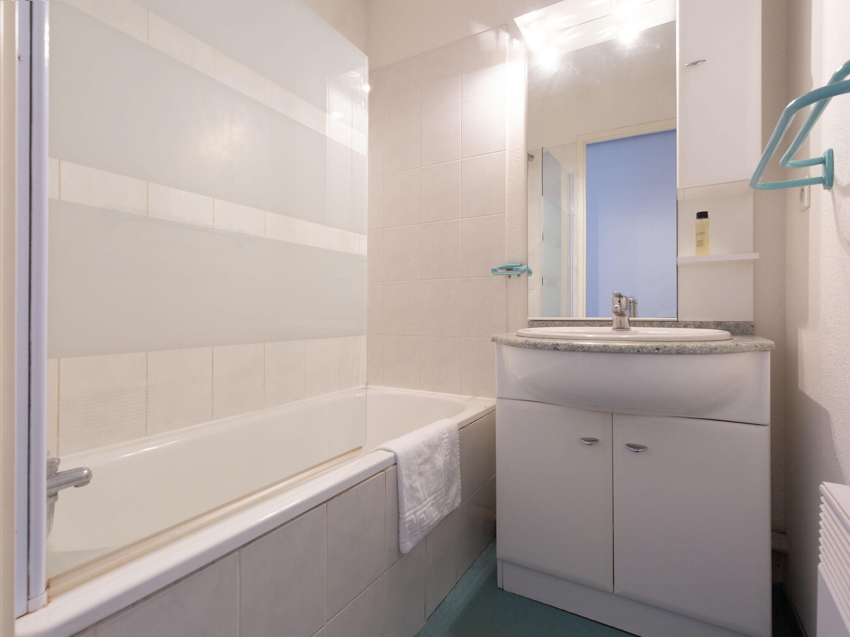 A bathroom with a bathtub, a sink, a mirror, and a towel rack.