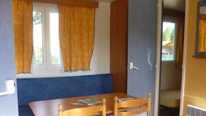 Ein Zimmer mit einem Holztisch, zwei Stühlen, einer blauen Bank und einem Fenster mit gelben Vorhängen.