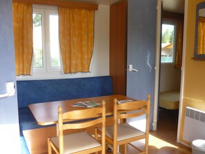 Ein Zimmer mit einem Holztisch, zwei Stühlen, einer blauen Bank und einem Fenster mit gelben Vorhängen.
