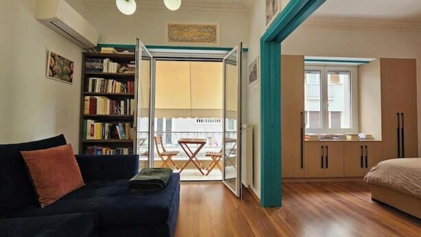 A room with a sofa, a bookshelf, a dining table with chairs, and a bed. - Cozy Suite in Kolonaki (Athens)