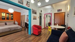 A compact living space with a bed, a red armchair, a yellow chair, a blue sofa, and a dining table. - Cozy Suite in Kolonaki (Athens)