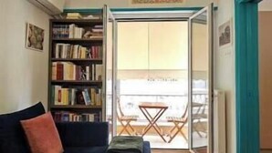 A living room with a dark blue sofa, a bookshelf, a ceiling light fixture, and a view through a glass door to an outdoor balcony. - Cozy Suite in Kolonaki (Athens)