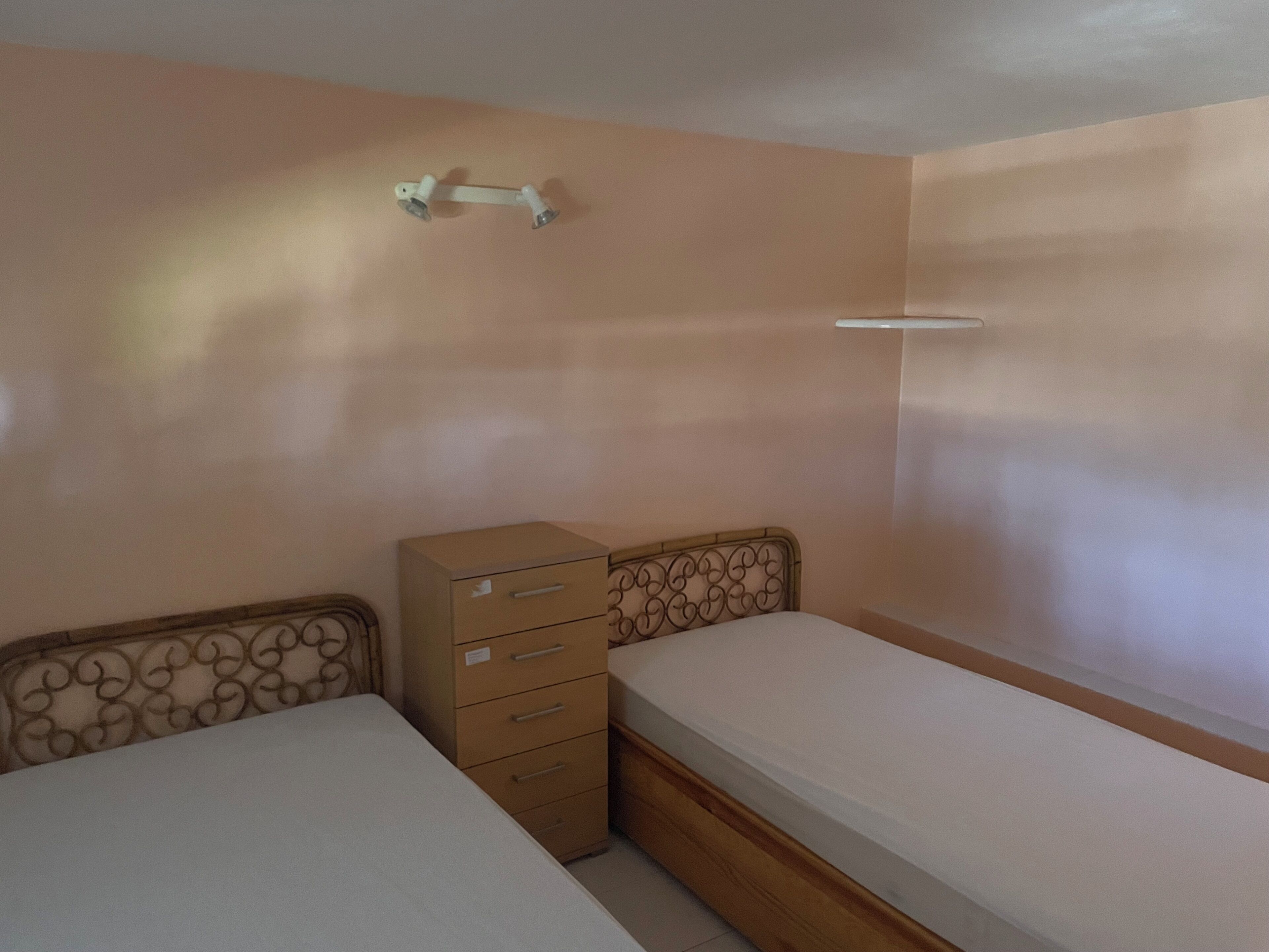 Een slaapkamer met twee eenpersoonsbedden, een houten dressoir met lades en een wandplank.