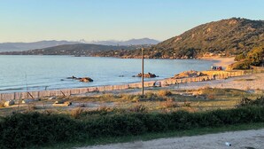 Un paisaje costero con una playa arenosa, afloramientos rocosos y un fondo montañoso.