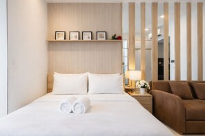 Ein Hotelzimmer mit Bett, Nachttisch, Lampe, Sofa und einer Wand mit gerahmten Bildern.