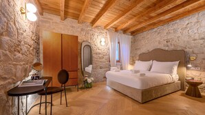 A bedroom with a stone wall, wooden ceiling beams, a bed, a desk, and a chair. - Balturio Boutique House (Kaštel Stari)