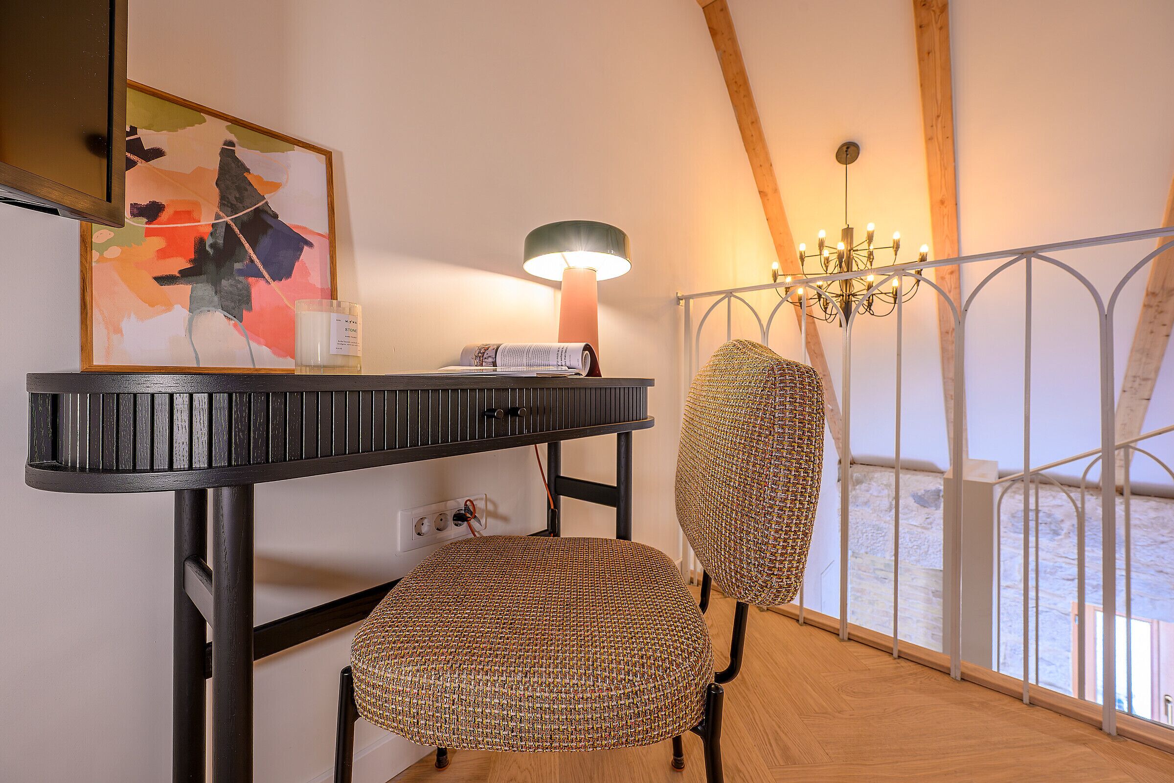 Ein Zimmer mit einem schwarzen Tisch, einem gewebten Stuhl, einer Lampe, einem Kronleuchter und einem Bild an der Wand.