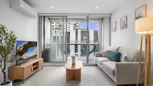 A modern living room with a television, a sofa, a coffee table, and a potted plant. - Marina-view 1-bed Apartment in Docklands (Melbourne)