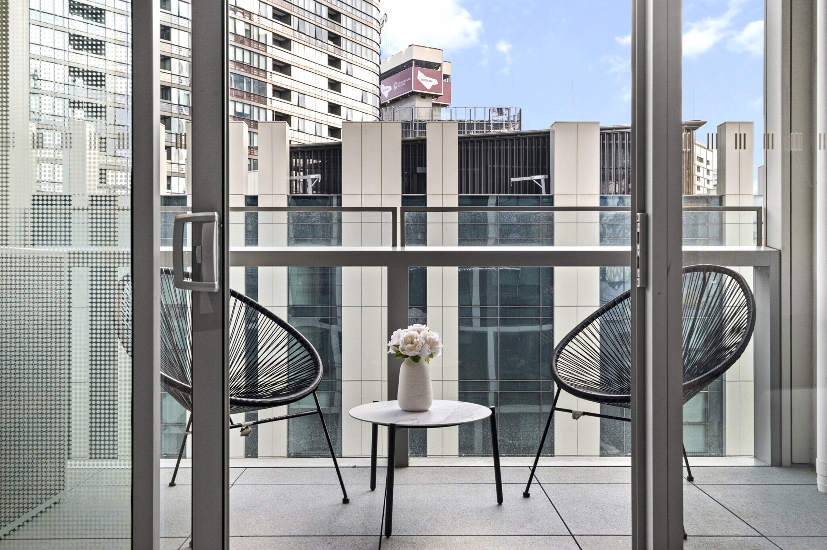Ein Balkon mit zwei Stühlen, einem kleinen Tisch und einem Blumenstrauß.