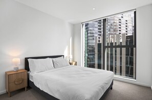A modern bedroom with a large window, a bed, a nightstand, and a lamp. - Marina-view 1-bed Apartment in Docklands (Melbourne)