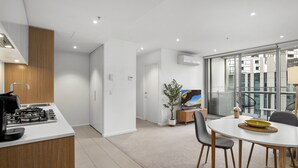 A modern kitchen with a gas stove, a dining area with a round table and chairs, and a large window offering a view of the city. - Marina-view 1-bed Apartment in Docklands (Melbourne)