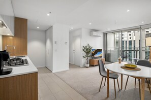 A modern kitchen with a gas stove, a dining area with a round table and chairs, and a large window offering a view of the city. - Marina-view 1-bed Apartment in Docklands (Melbourne)