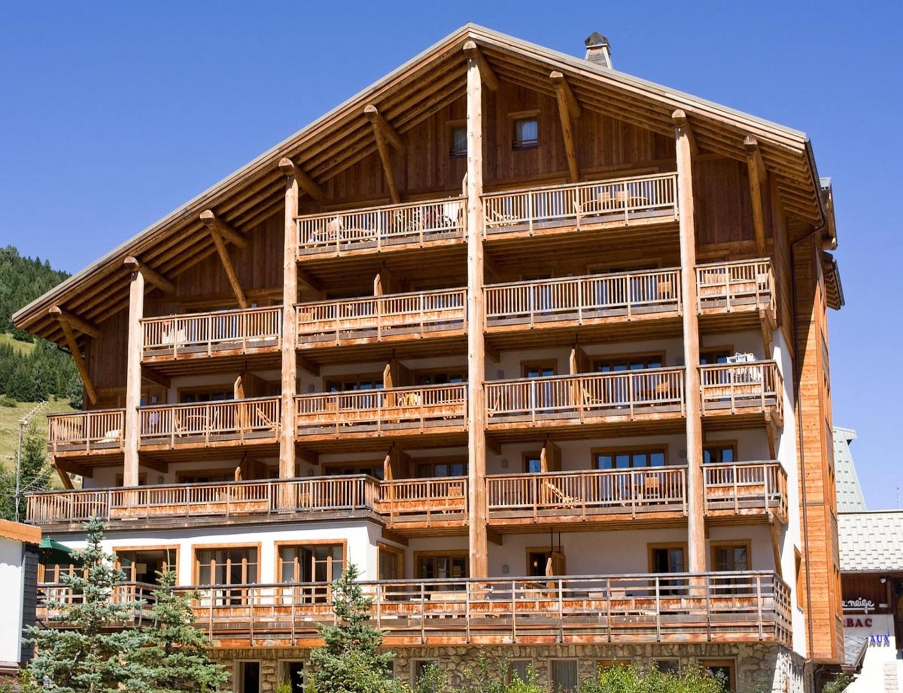 A multi-story wooden building with balconies, a stone base, and a clear sky.