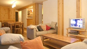 A cozy living room with a wooden dining table, a sofa, and a television on a wooden stand. - Alpine Apartment With Beautiful Views (Les Deux Alpes)