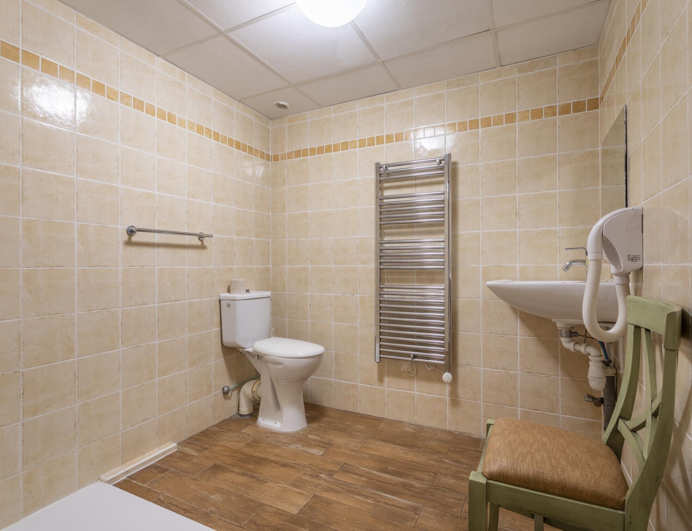Ein Badezimmer mit Toilette, Handtuchhalter, Waschbecken und einem Stuhl.